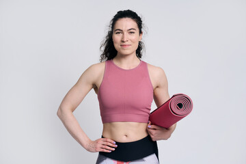 Confident young fit woman carrying yoga mat, smiling looking at camera, isolated on white background