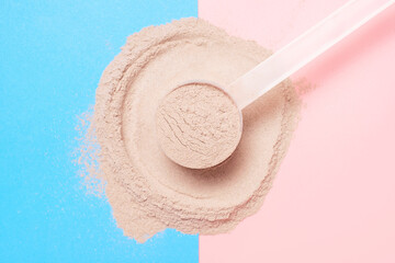 Scattered protein and measuring spoon on blue and pink background top view, concert of sports...