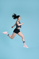 Fototapeta na wymiar Cheerful competitive sportswoman, female runner jogging marathon isolated over blue color background