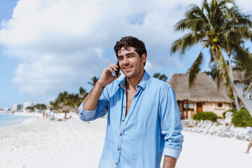 hispanic young man talking by mobile phone at the beach on vacations or holidays in Mexico Latin...