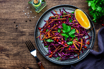 Coleslaw red cabbage salad with carrot, parsley, pomegranate and orange  with olive oil dressing on wooden kitchen table background, top view