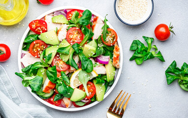 Chicken and vegetables salad with tomatoes,  avocado, cucumber, onion, lamb lettuce and sesame seeds on gray table background, top view