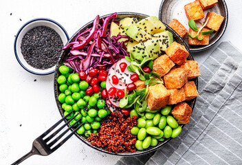 Healthy vegan food. Buddha bowl with quinoa, fried tofu, avocado, edamame, green peas, radish, cabbage and sesame seeds. White kitchen table background, top view - obrazy, fototapety, plakaty