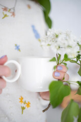 A cup of morning coffee in female hands and flowers on a white background