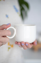 A cup of morning coffee in female hands and flowers on a white background