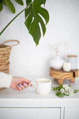 A cup of morning coffee in female hands and flowers on a white background