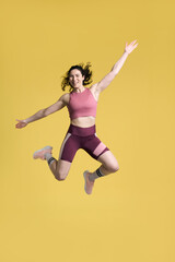 Fototapeta na wymiar Full length portrait smiling athletic woman, jumping high up over yellow isolated background. Sport