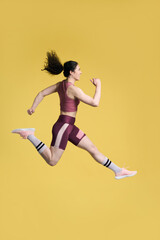 Fototapeta na wymiar Side portrait of determined woman jogger in pink top and shorts, running over yellow background