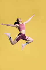 Fototapeta na wymiar Determined confident young sportswoman, athlete jumping high up, succeed training on yellow backdrop