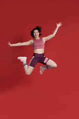 Fototapeta na wymiar Full length studio portrait of female athlete jumping over red background. Sport Fitness Workout