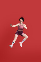 Fototapeta na wymiar Full length portrait young athletic woman performing a martial arts kick, isolated on red background