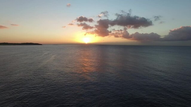 Drone down over ocean to reveal rocks as sun rises in the back ground.