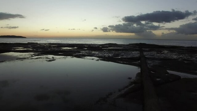 Drone over rock pools out to sea as the dawn breaks.