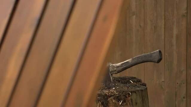 Used fire wood cutting or chopping axe sits in log stump revealed 4k slow motion shot in backyard between wooden fence and outdoors chair.