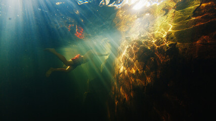 Young man free dives in the lake located in a forest