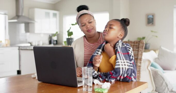 Unaltered african american mother and sick daughter using laptop for doctor video call, slow motion