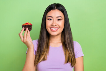 Photo portrait of lovely young vietnamese chinese lady hold tasty cupcake dressed stylish violet garment isolated on green color background