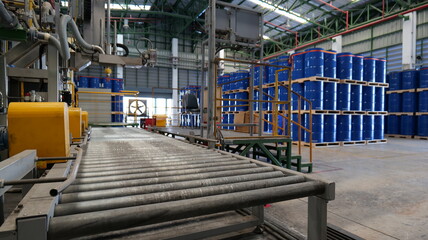 Drums holding 200 liters of chemicals are filled on a line. Inside the warehouse, stacks of blue...