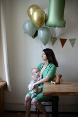 A mother at her child's birthday party breastfeeds a toddler against the background of balloons