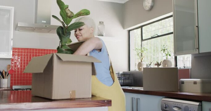 Happy biracial woman unpacking plant from carton at home in slow motion
