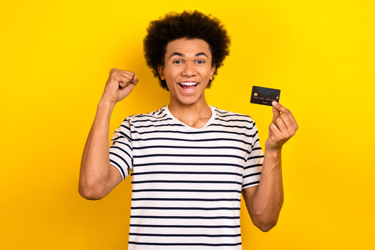 Portrait photo of youngster crazy triumphant businessman fist up hold credit card eshopping advantage isolated on yellow color background