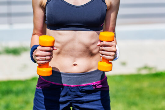 Close-up of a young woman in short sport clothes working out with orange color dumbbells focus on hands 