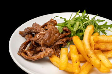 Stir-fried beef served with french fries and arugula leaves on white plate, isolated on black background. Close up view.