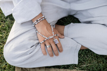 partial view of man with mala beads sitting in easy yoga pose and meditating outdoors