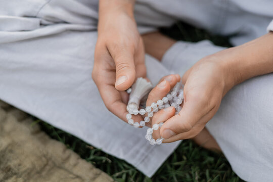 cropped view of young man holding mala beads while meditating outdoors