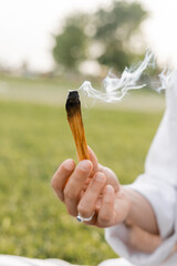 selective focus of smoldering palo santo stick in hand of cropped yoga man