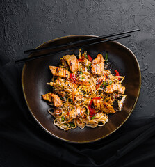 Stir fry noodles with vegetables and chicken in a black bowl