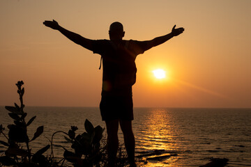 Fototapeta premium Man stand with arms wide open on beach and look at water. Traveler spend past day close to waves, watch sunset.