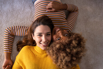 Top view of lovely multiracial lesbian couple lying on a carpet looking at camera. Beautiful happy...