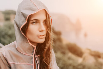 Fototapeta premium Woman rain umbrella. Happy woman portrait wearing a raincoat with transparent umbrella outdoors on rainy day in park near sea. Girl on the nature on rainy overcast day.
