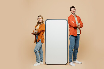 Full body fun young couple two friends family man woman wear casual clothes together stand near big huge blank screen mobile cell phone smartphone with area isolated on pastel plain beige background.