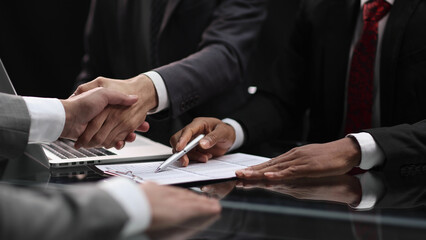 Obraz premium businessmen shaking hands, after concluding a modern cooperation agreement in the office and financial paper graphics on the table