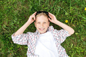 A cute boy lies in the grass and smiles, holds sunglasses on his head