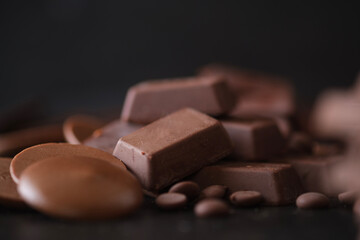 Chocolate button, chocolate cubes and chocolate chips on dark background.