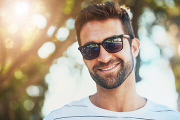 Sunglasses, casual and portrait of a happy man in an outdoor park while on a vacation, adventure or holiday. Smile, confidence and young male person with eyewear standing in a garden on weekend trip.