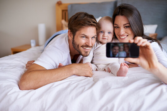 Mother, father and smile for selfie with baby on bed in home for love, care or social media together. Happy family, parents and cute kid taking photograph for memory, happiness and relax in bedroom