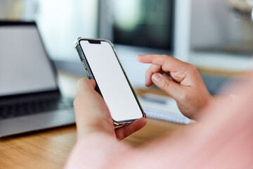 A woman sitting with a blank white screen mobile phone and laptop, indoors.