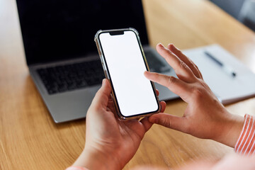 A female touching a blank white screen of her mobile phone in front of the laptop.