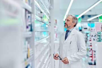 Side profile of a man looking at the shelf with medicine, working as the pharmacist.