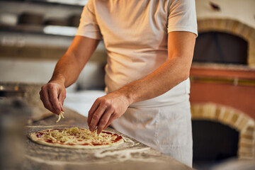 Close-up of a pizza master, making a pizza for his customers, putting cheese on top.