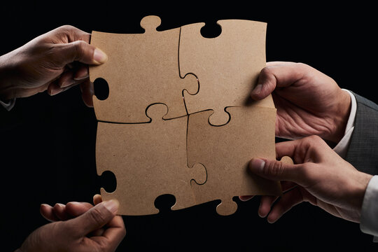Close-up of business partners putting together three white puzzl