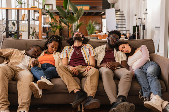 Party multiracial friends, drunk and hungover sleeping on a sofa in the living room after the celebration. Drinking, hangover and alcohol, coworking workers at break sleeping on the sofa