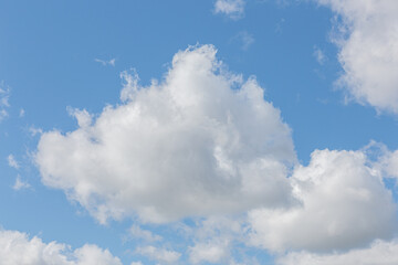 White fluffy clouds on a summer blue sky in cartoon style for background or wallpaper design. The background is white of round clouds in a blue sky.