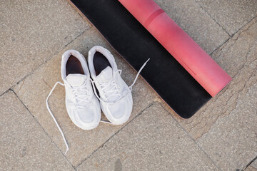 Top view of white sneakers and pink fitness mat on sidewalk outdoors