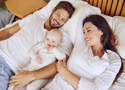 Top view of mother, father and baby on bed for love, care and quality time together. Happy parents, family and newborn kid relaxing in bedroom with support, childhood development and bonding at home