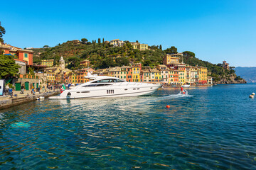 Fototapeta premium Cityscape and port of Portofino with a luxury yacht moored. Tourist resort in Genoa Province, Liguria, Italy, Europe. Colorful houses, Mediterranean sea (Ligurian sea).